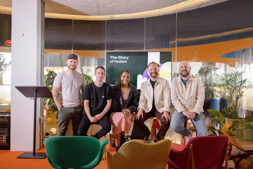 Five people posed in front of a screen displaying “The Story of Notion” in a colourful, modern office space with plants, vibrant furniture, and a relaxed atmosphere.
