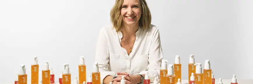 Person smiling at a table filled with Pai Skincare products, arranged in neat rows against a plain white background.