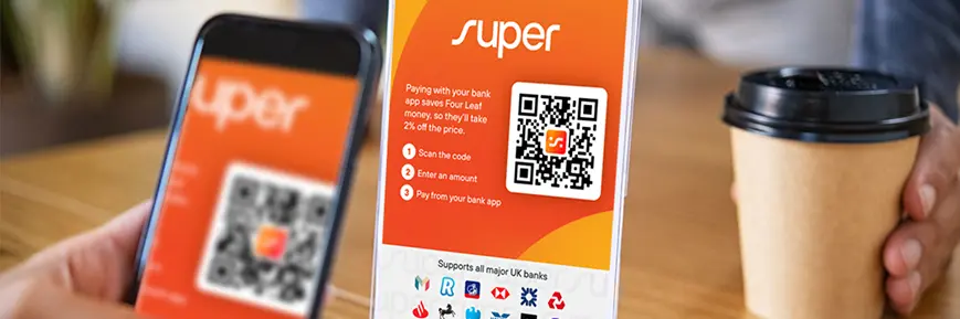 Smartphone scanning a QR code on a “Super” payment sign at a café table, with a takeaway coffee cup and blurred hand in the background.