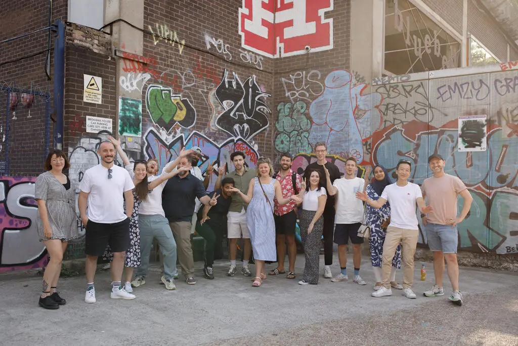 Group of LeftBrain staff posing cheerfully in front of a brick wall covered in colourful graffiti.