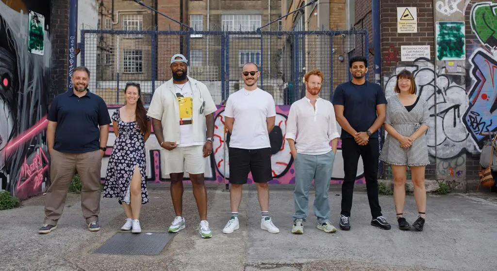A group of seven LeftBrain team members standing together in an urban setting with graffiti-covered walls and industrial buildings in the background, smiling at the camera.