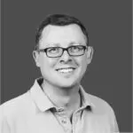 Black-and-white headshot of a smiling person wearing glasses and a collared shirt against a plain background