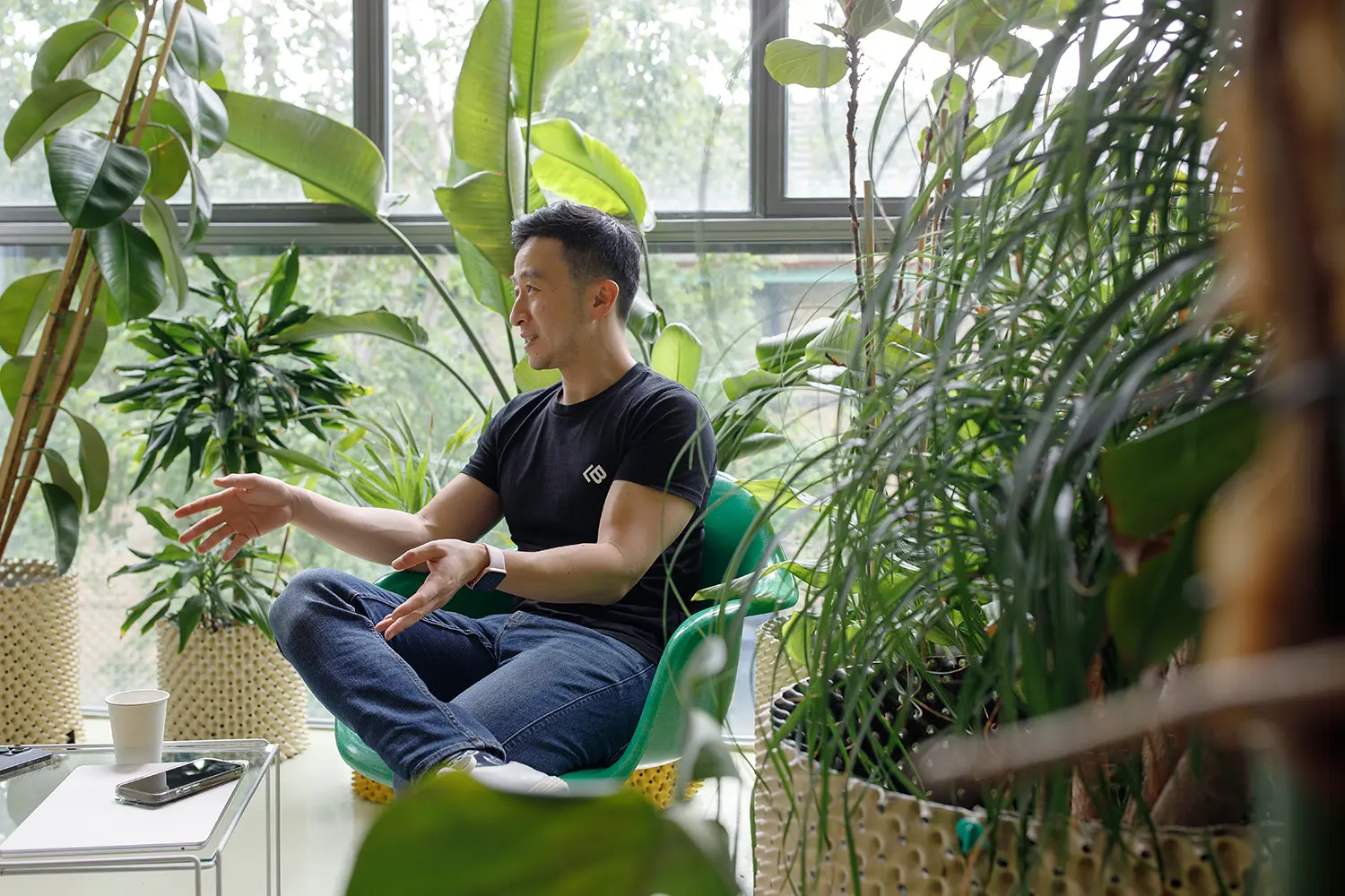 Michael in conversation with someone in a well lit office space filled with plants.