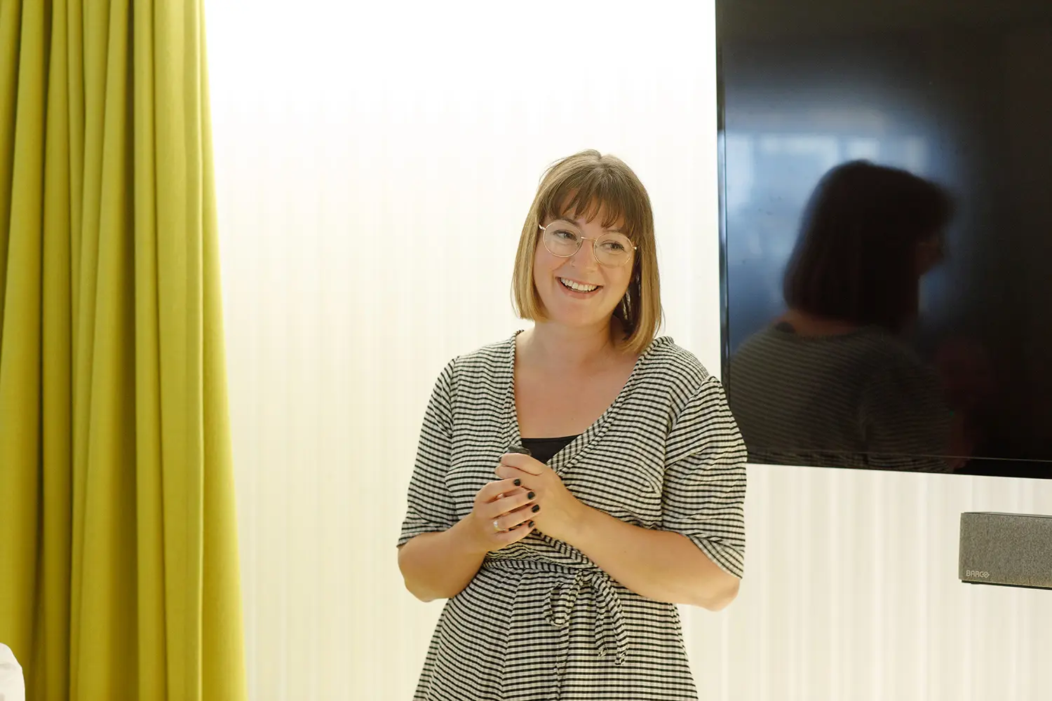 Smiling female stood infront of a television in a meeting room setting