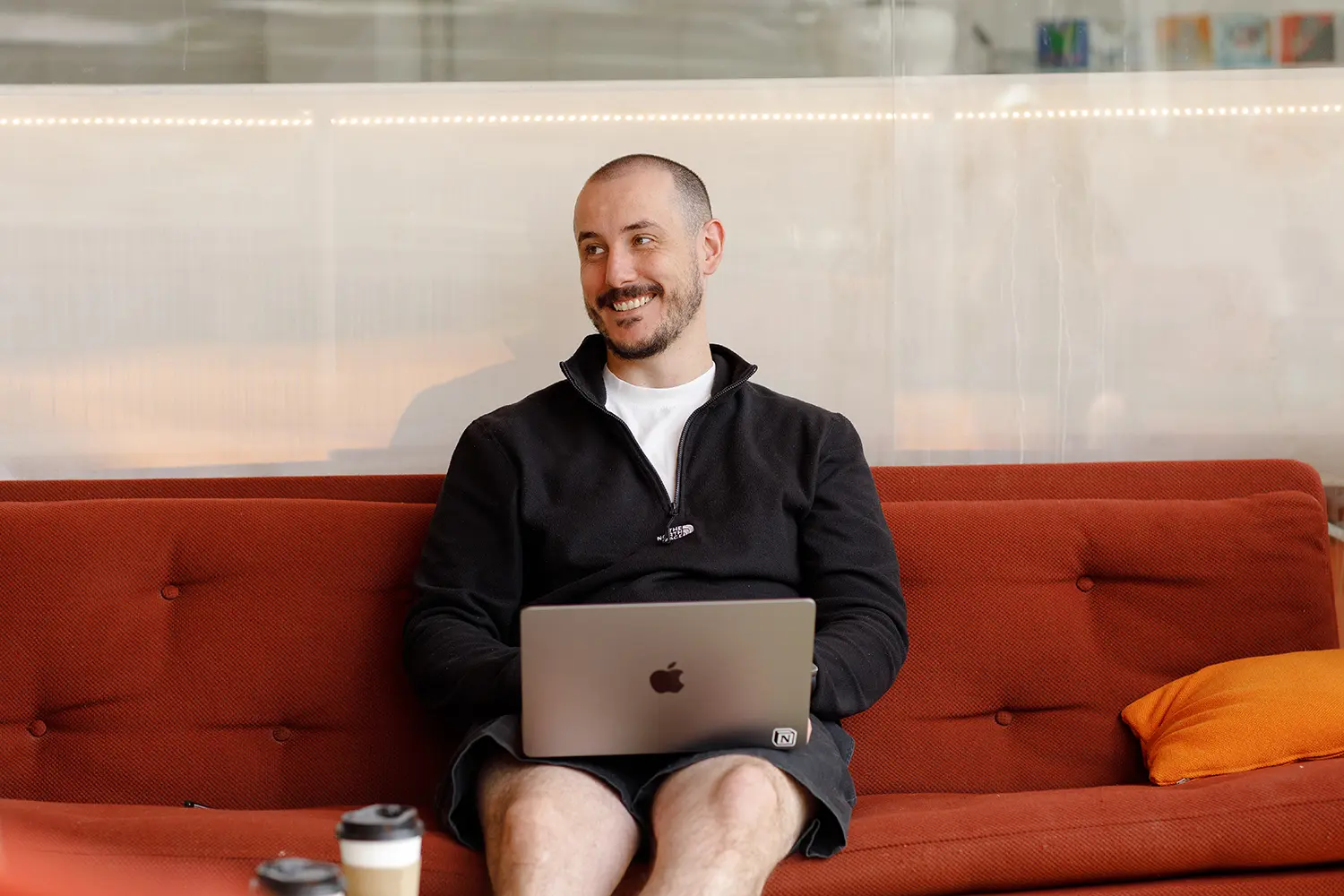 Man sat on a couch with a laptop in an office space smiling