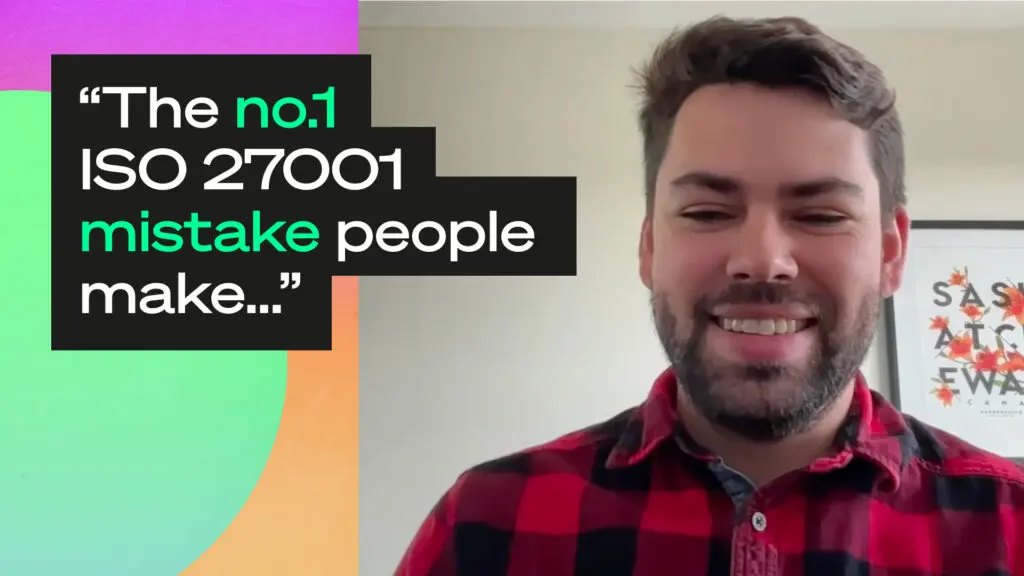Video thumbnail: a smiling person with short dark hair and a beard, wearing a red and black checked shirt, on a video call in a room with a framed poster behind them. A quote on the left of the frame reads: "The no.1 ISO 27001 mistake people make…"