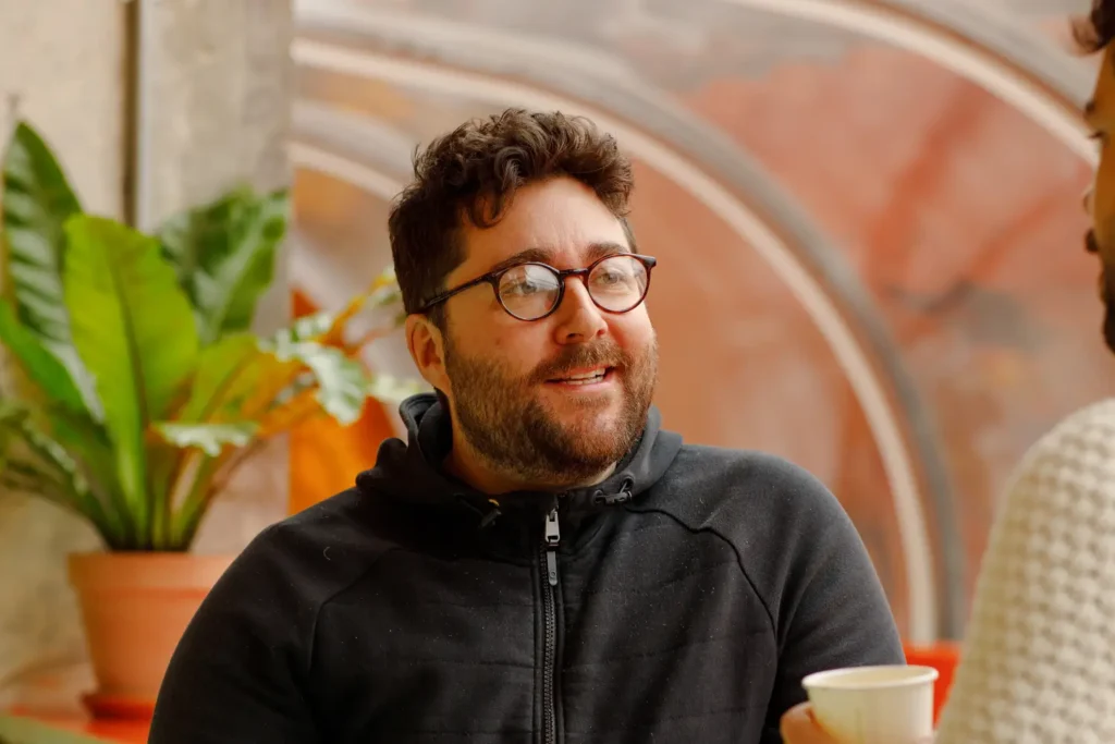 Head and shoulders image of LeftBrain's Matthew Bensley speaking to another colleague in an office setting with greenery in the background.