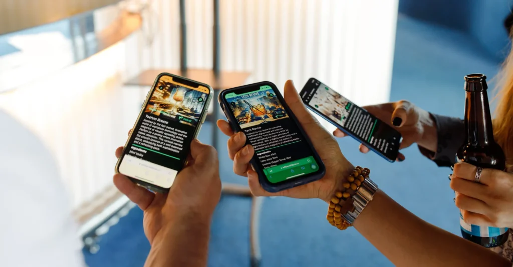 Close-up of three hands holding smartphones, each displaying different AI-generated cocktail recipes with vibrant images and descriptions; one hand also holds a beer bottle, suggesting a casual social setting.