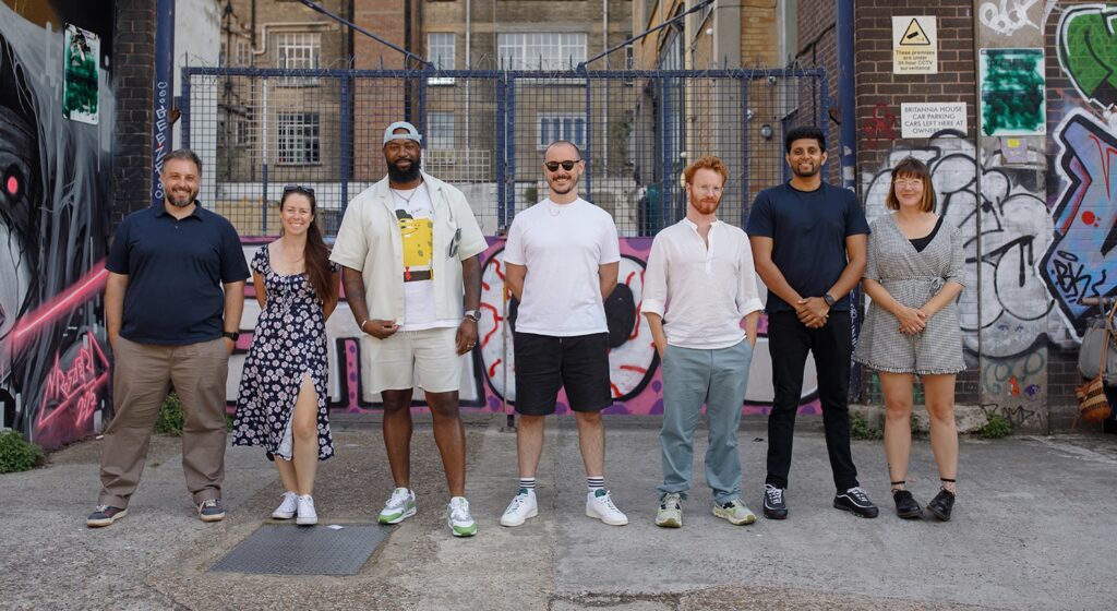 A group of seven LeftBrain team members standing together in an urban setting with graffiti-covered walls and industrial buildings in the background, smiling at the camera.
